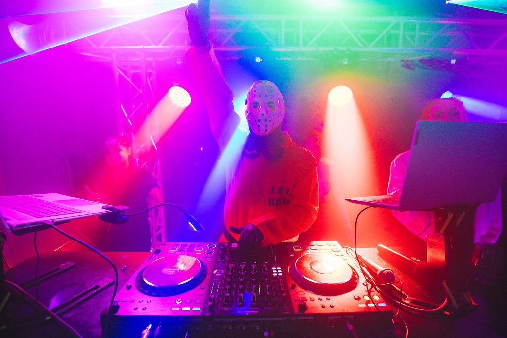 Masked DJ performing under colourful stage lights at a MoDJs show